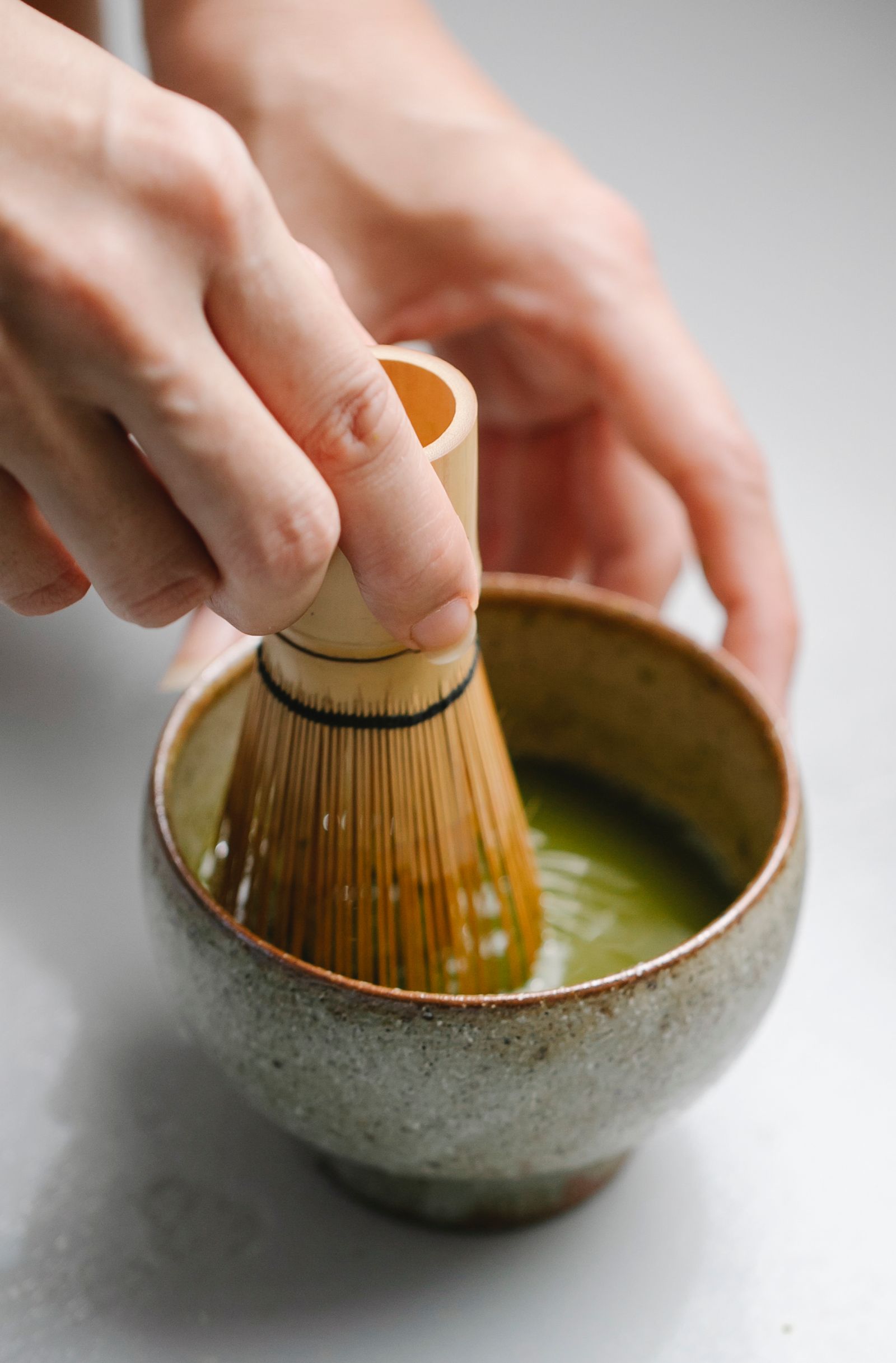 Hands whisking matcha in a ceramic bowl